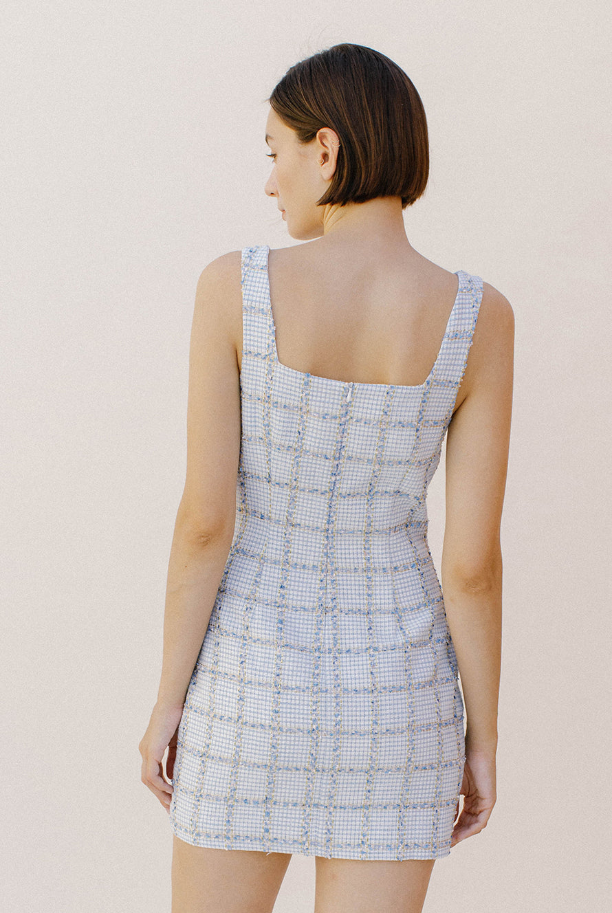 Back view of a woman wearing a light blue tweed dress against a plain background