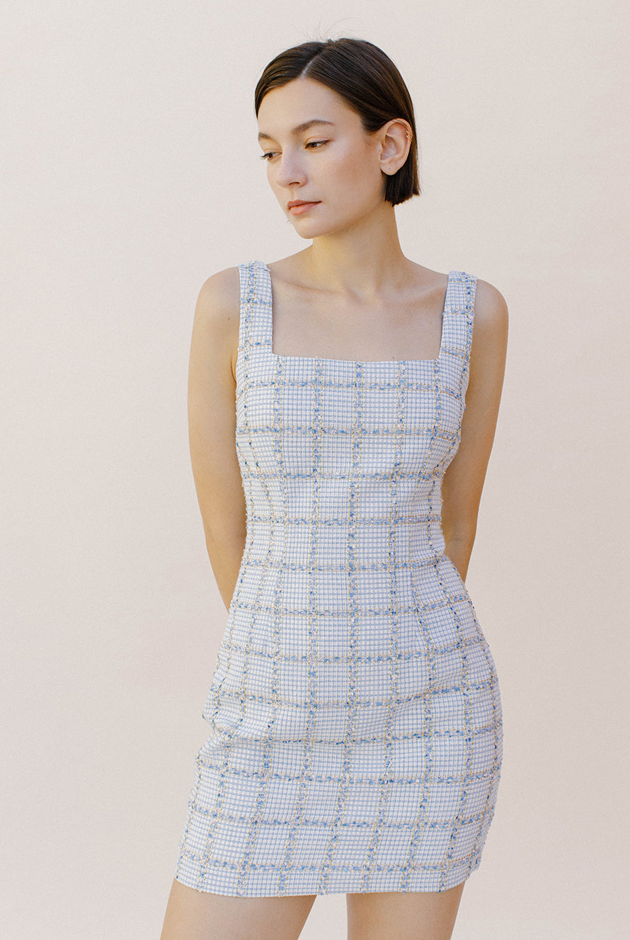 Woman wearing a light blue tweed dress against a plain background