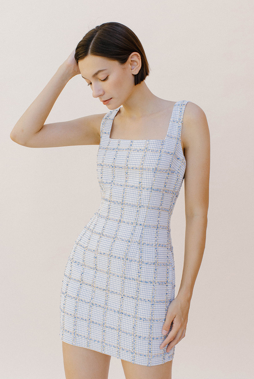 Side view of a woman wearing a light blue tweed dress against a plain background