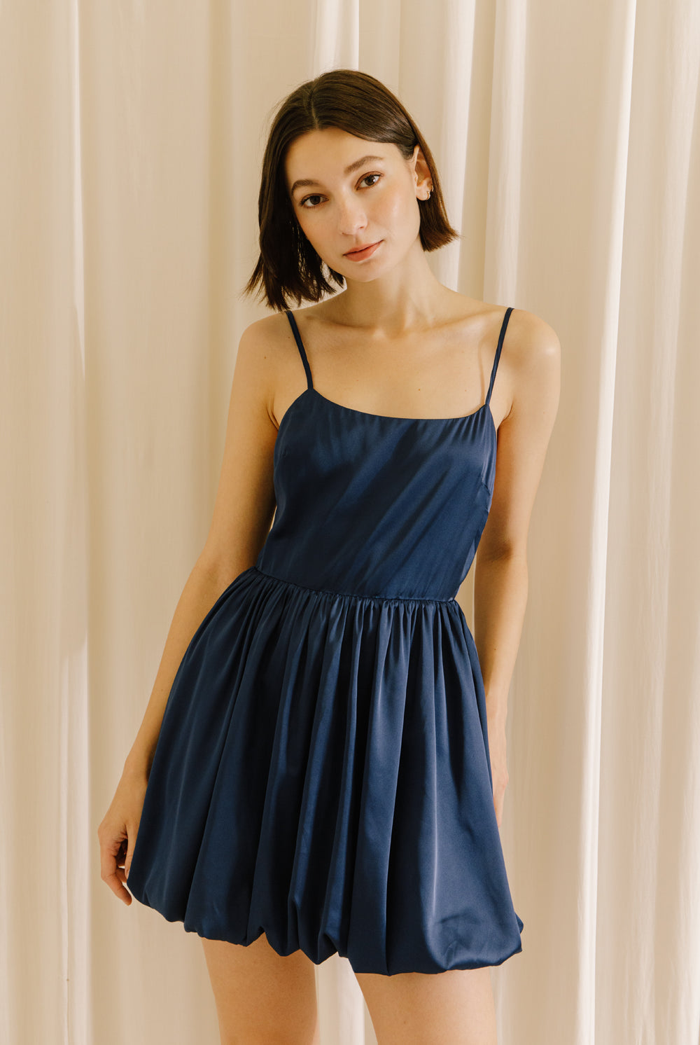 Woman wearing a navy blue dress against a beige curtain background