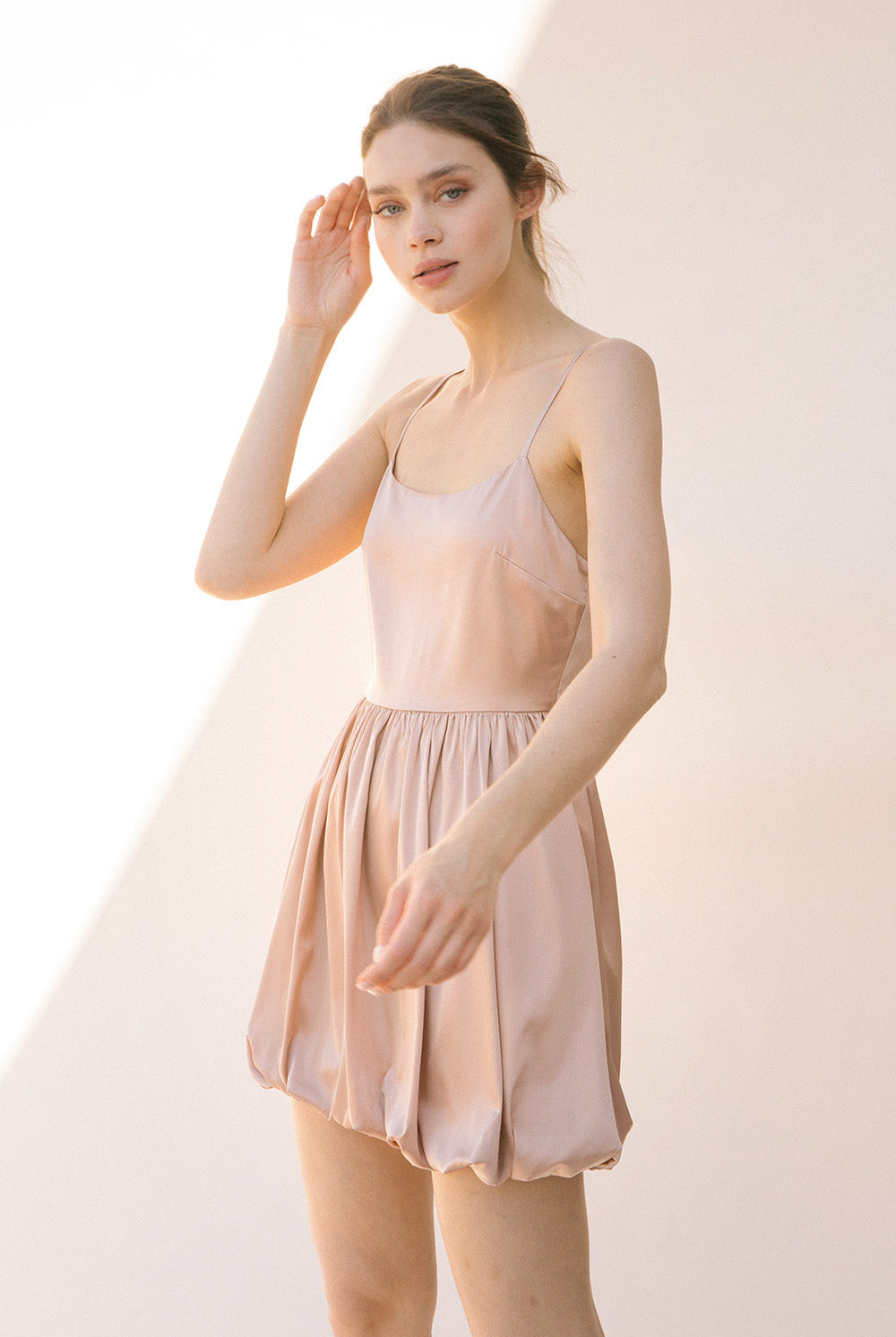 Side view of a woman wearing a sheer beige dress against a plain background