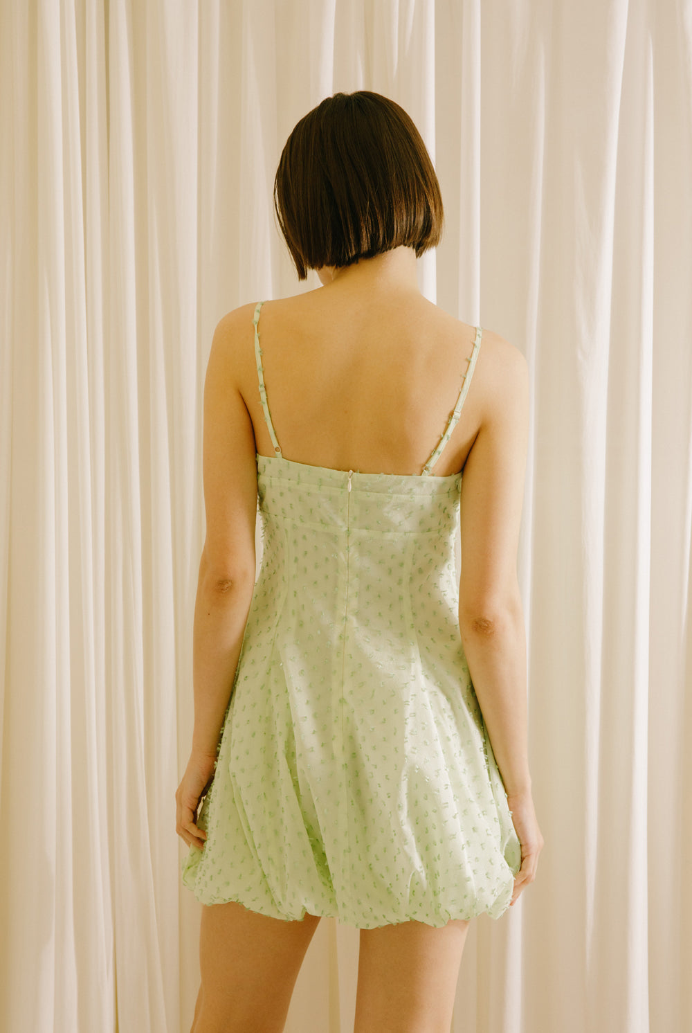 Back view of a woman wearing a mint polka dot mini dress against a white background