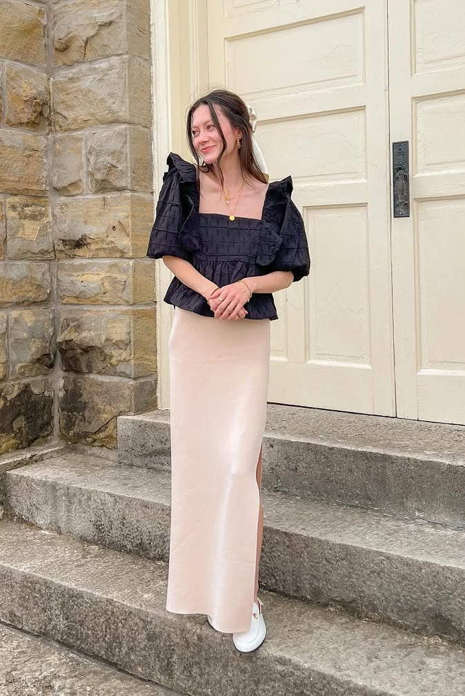 Woman wearing a black blouse standing on steps in front of a large door.
