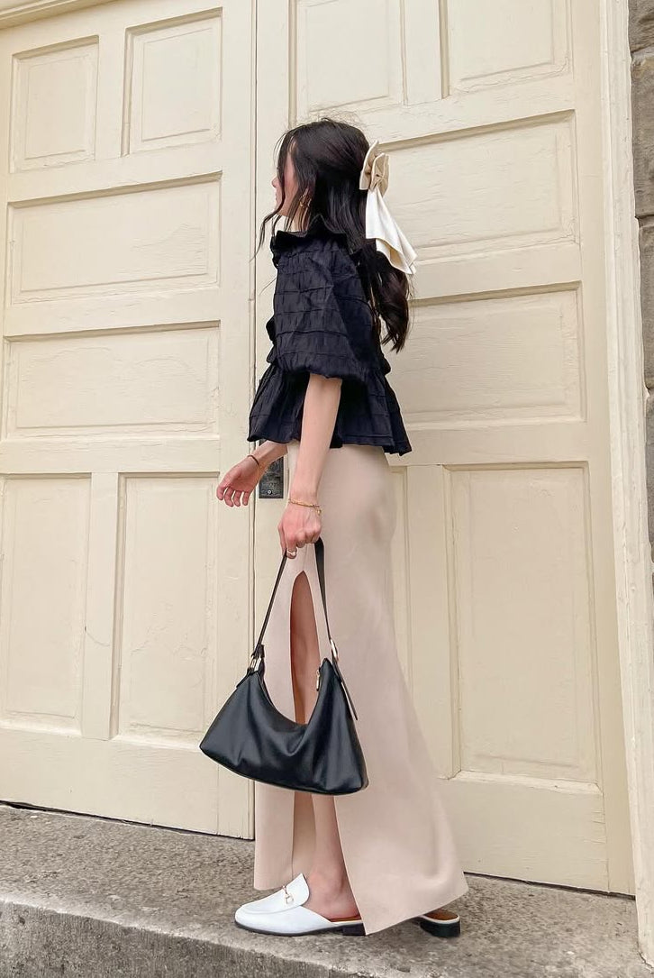 Side of a woman wearing a black blouse standing on steps in front of a large door.