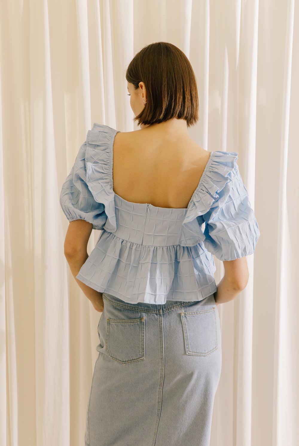 A back view of a model wearing a blue top with a back invisible zipper and a light denim midi skirt