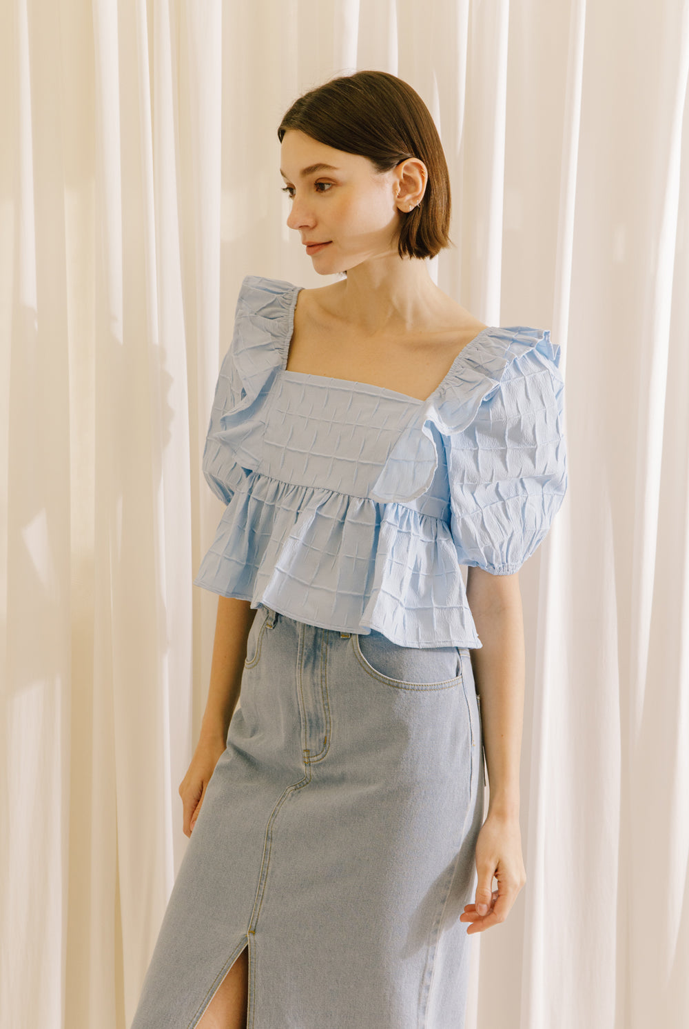 Side view of a model wearing a blue top with a back invisible zipper and a light denim midi skirt