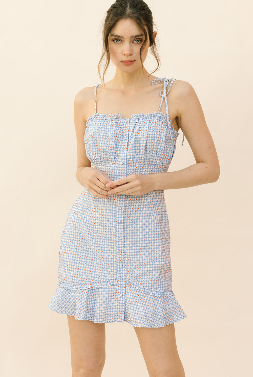 Woman wearing a blue checkered dress with small red daisy print on a beige background