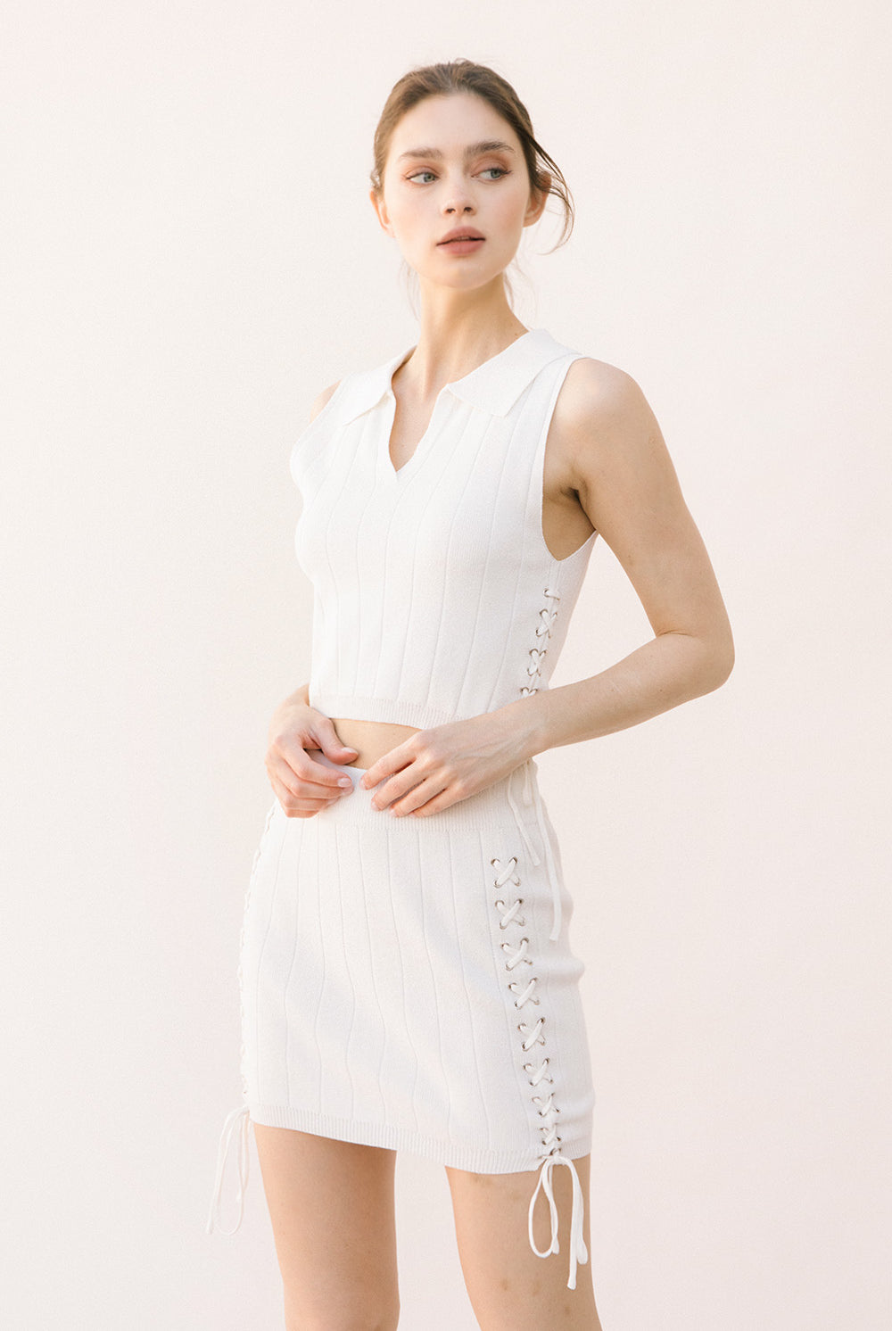Woman wearing a white sleeveless top and skirt set with lace-up on the side on a light background
