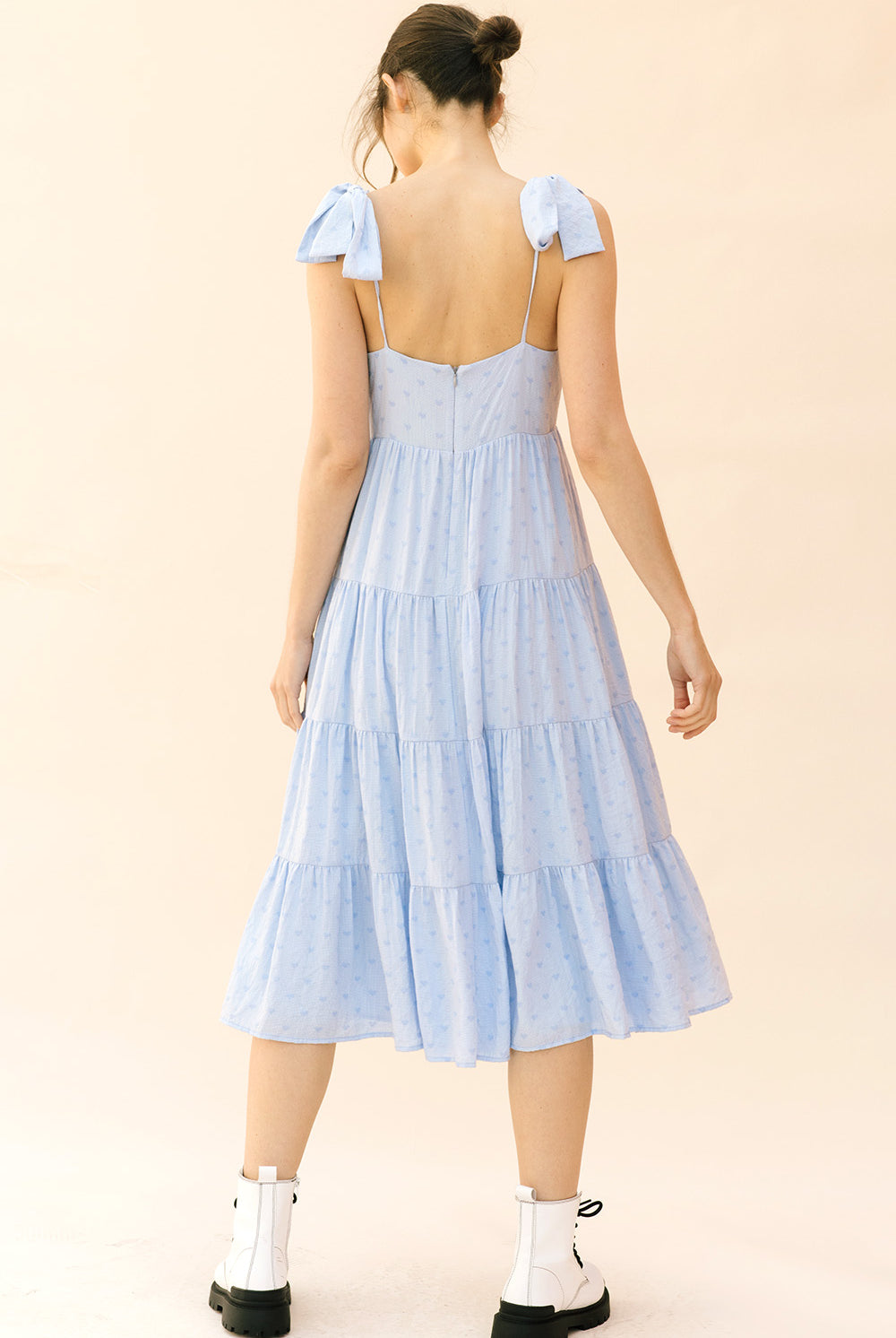 Back view of a woman wearing a light blue dress with ruffled sleeves on a beige background