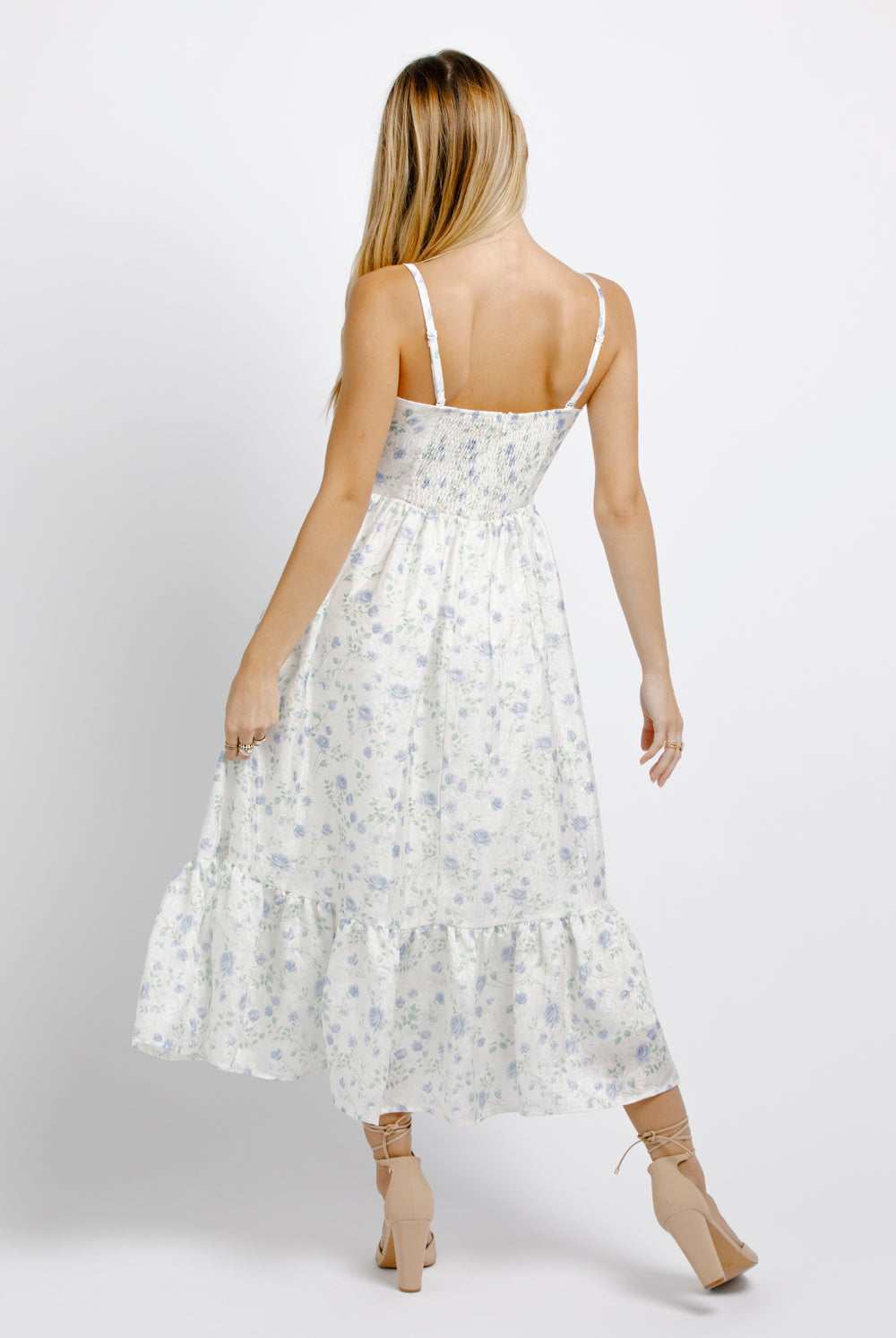Back view of a woman wearing a white and blue floral dress on a plain background