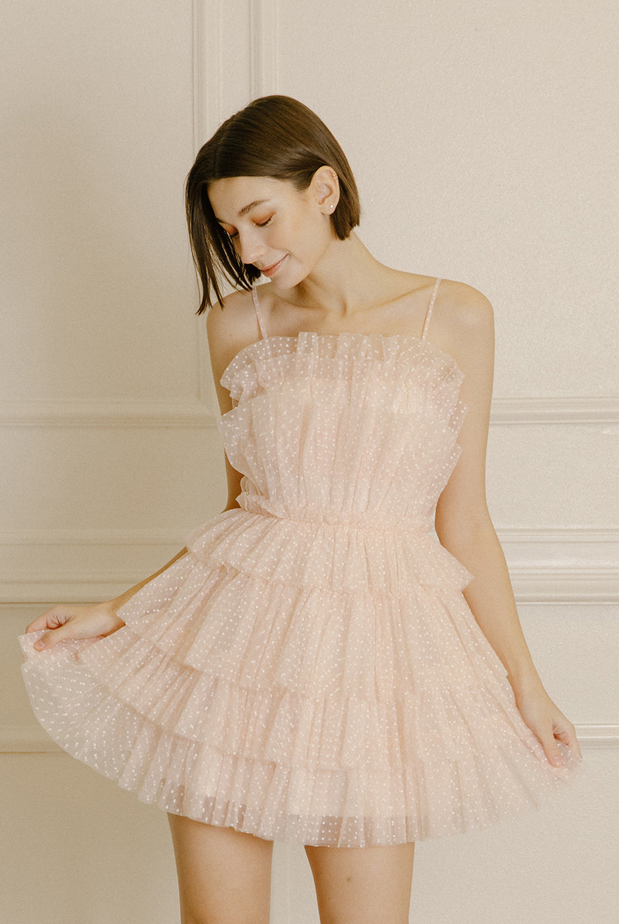 Woman wearing a soft pink mini dress with white dots and tiered tulle on a beige background