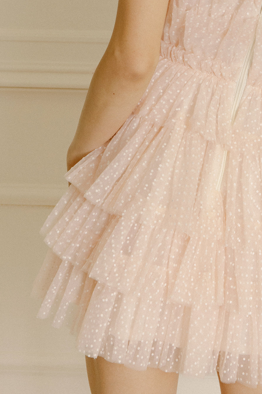 Details of a soft pink mini dress with white dots and tiered tulle on a beige background