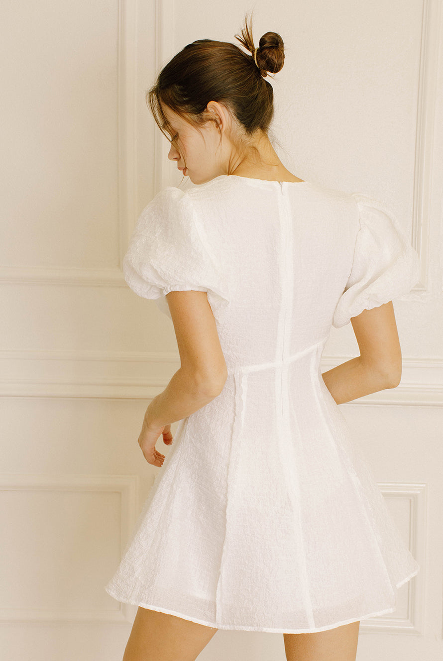 Back view of a woman wearing a white dress against a light-colored wall