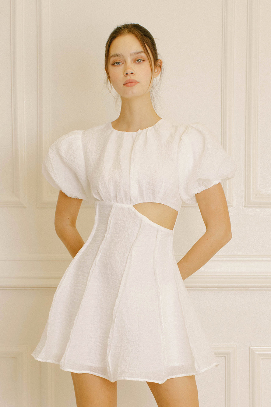 Woman wearing a white mini dress with cut-out design against a neutral background
