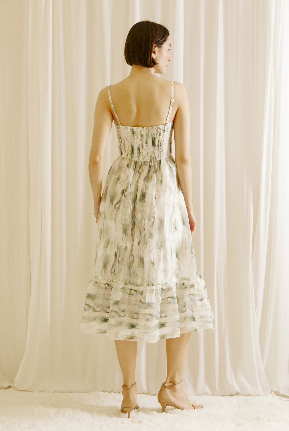 Back view of a woman wearing a green and blue tie dye effect dress standing against a plain background
