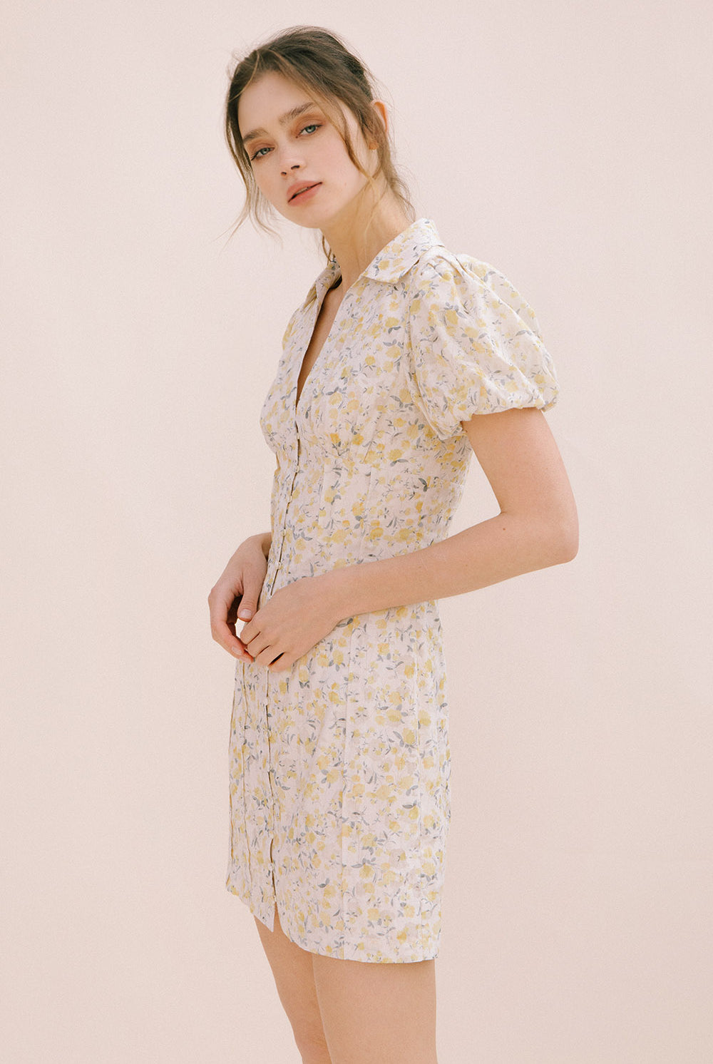 A woman modeling a cream dress with a floral pattern, short puff sleeves and a bodycon fitted body.