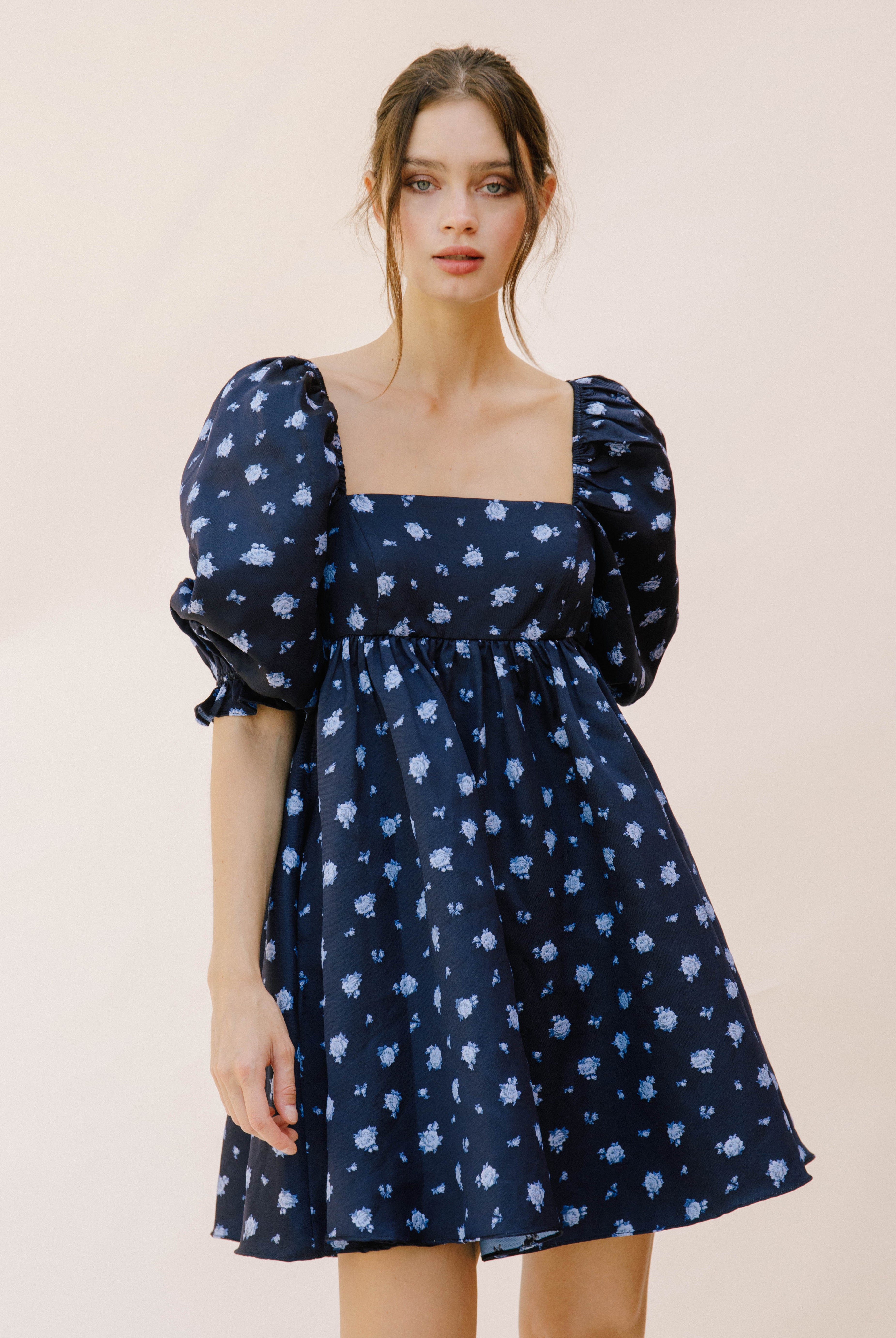 Woman wearing a navy blue dress with puff sleeves and floral pattern on a beige background