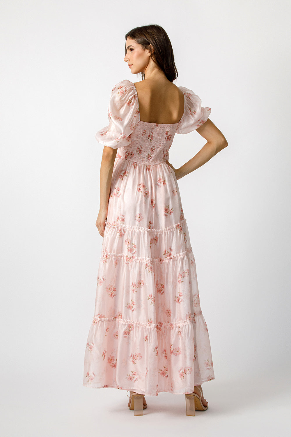 Back view of a woman wearing a pink floral dress on a white background