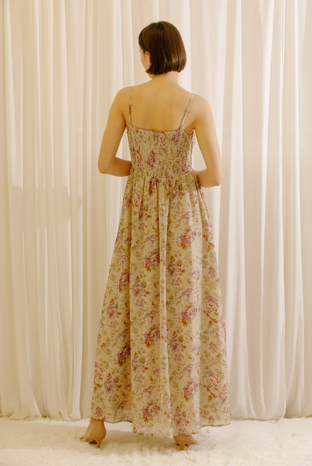 A woman viewed from behind wearing a maxi dress with a romantic floral print, adjustable straps and a flowy maxi silhouette.