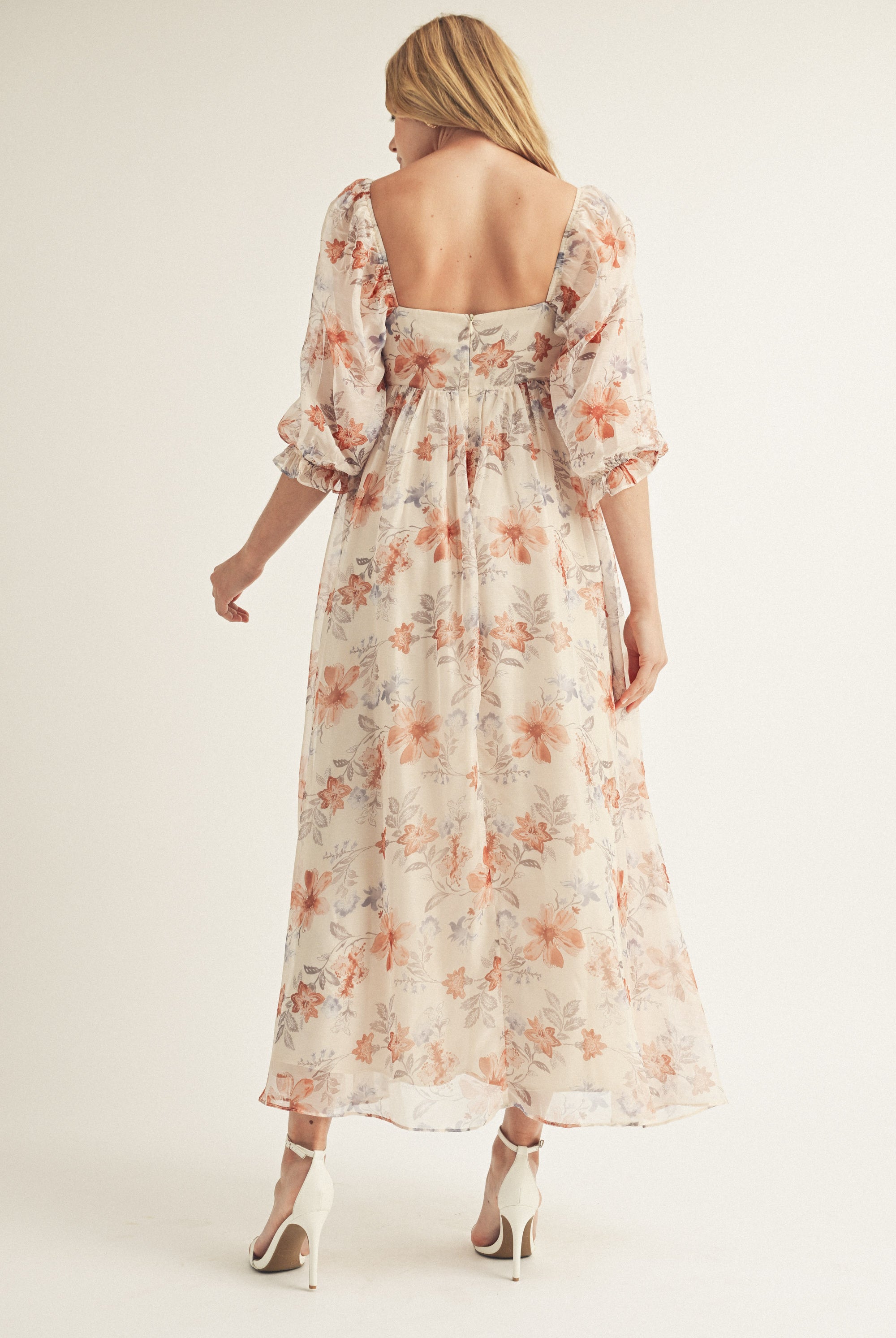 Back view of a woman wearing a beige floral dress with a plain background