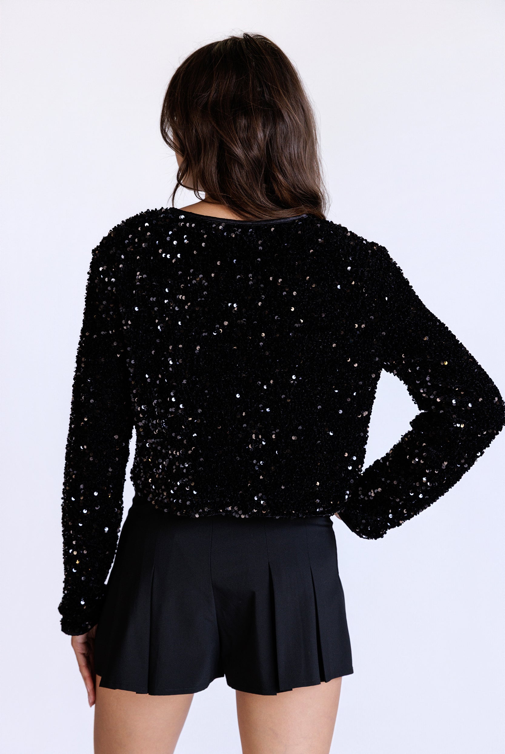 Back view of a model wearing a black sequin jacket and black shorts on a white background