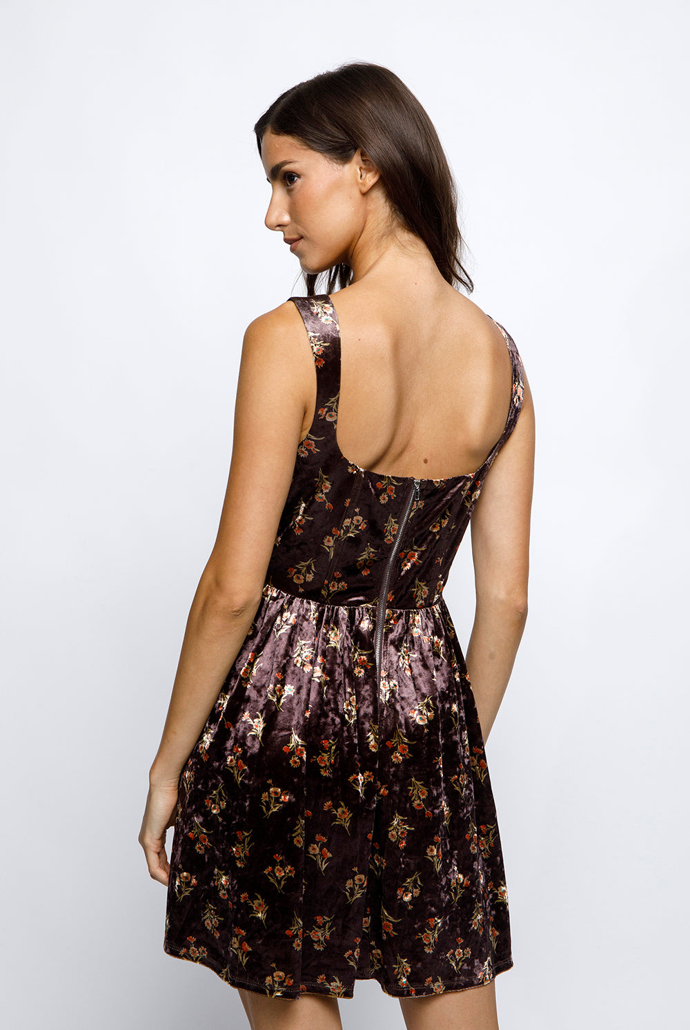 Back view of a woman wearing a brown floral velvet mini dress on a white background