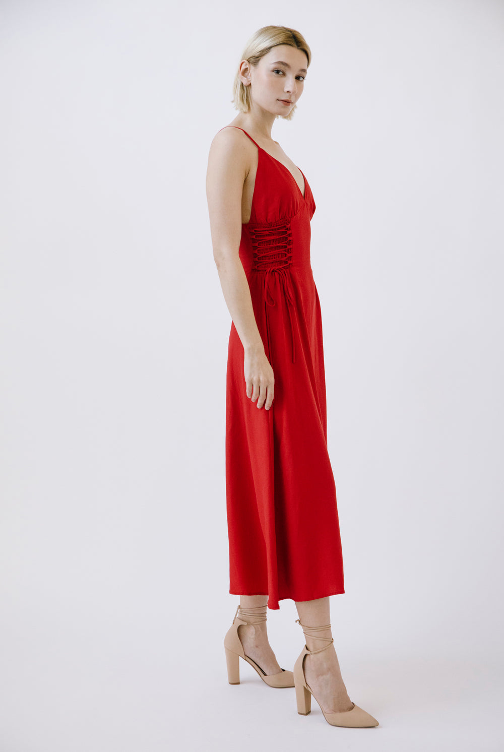 Side view of a woman wearing a red dress with beige shoes on a white background