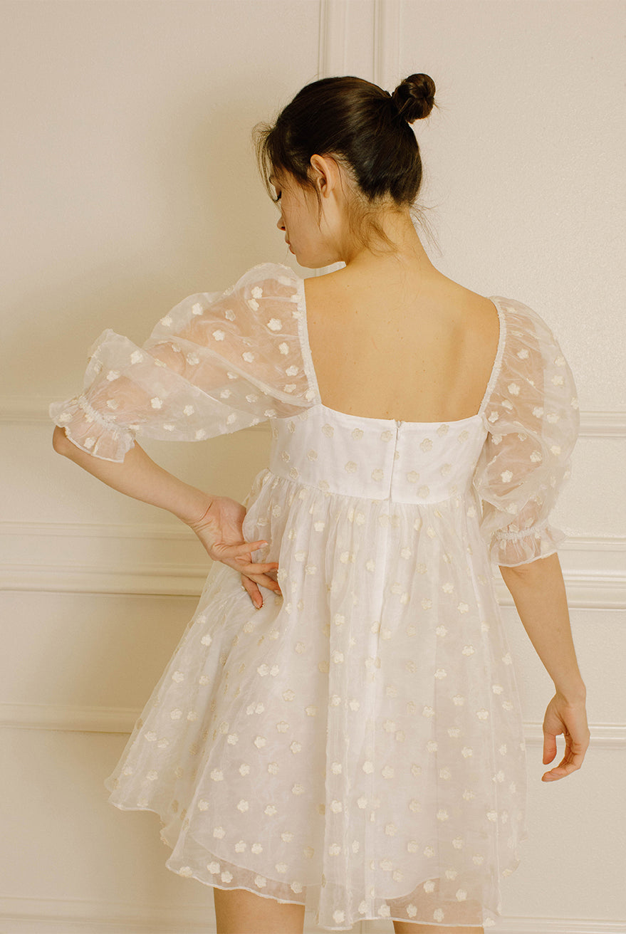 Back view of a woman in a cream polka dot dress against a neutral wall