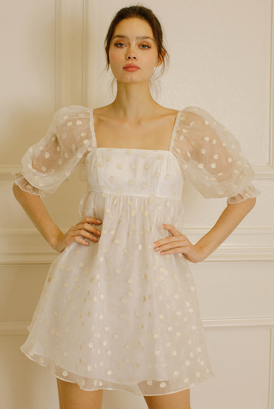 Woman in a cream polka dot dress against a neutral wall