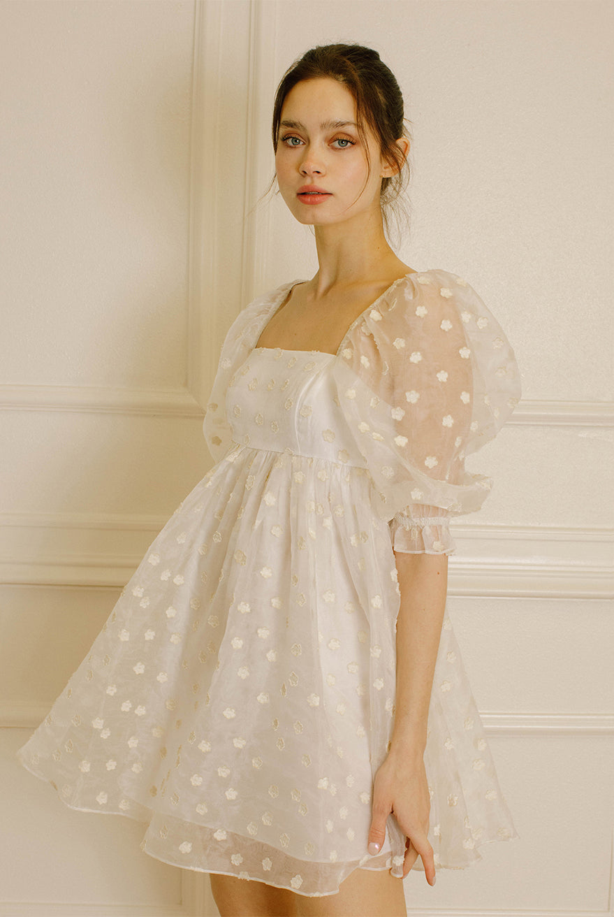 Side view of a woman in a cream polka dot dress against a neutral wall