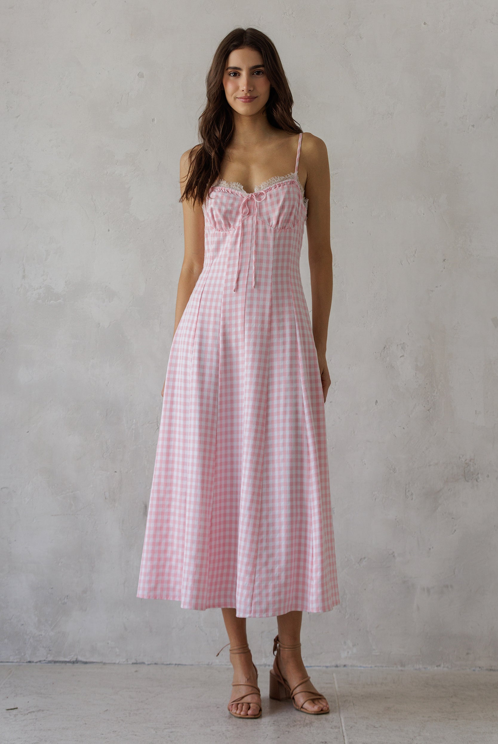 Woman wearing a soft pink gingham pattern midi dress against a grey wall