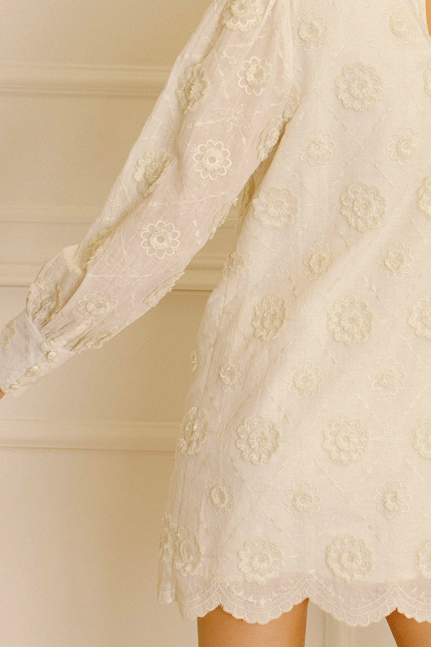 Cream daisy embroidery mini dress against a neutral wall.