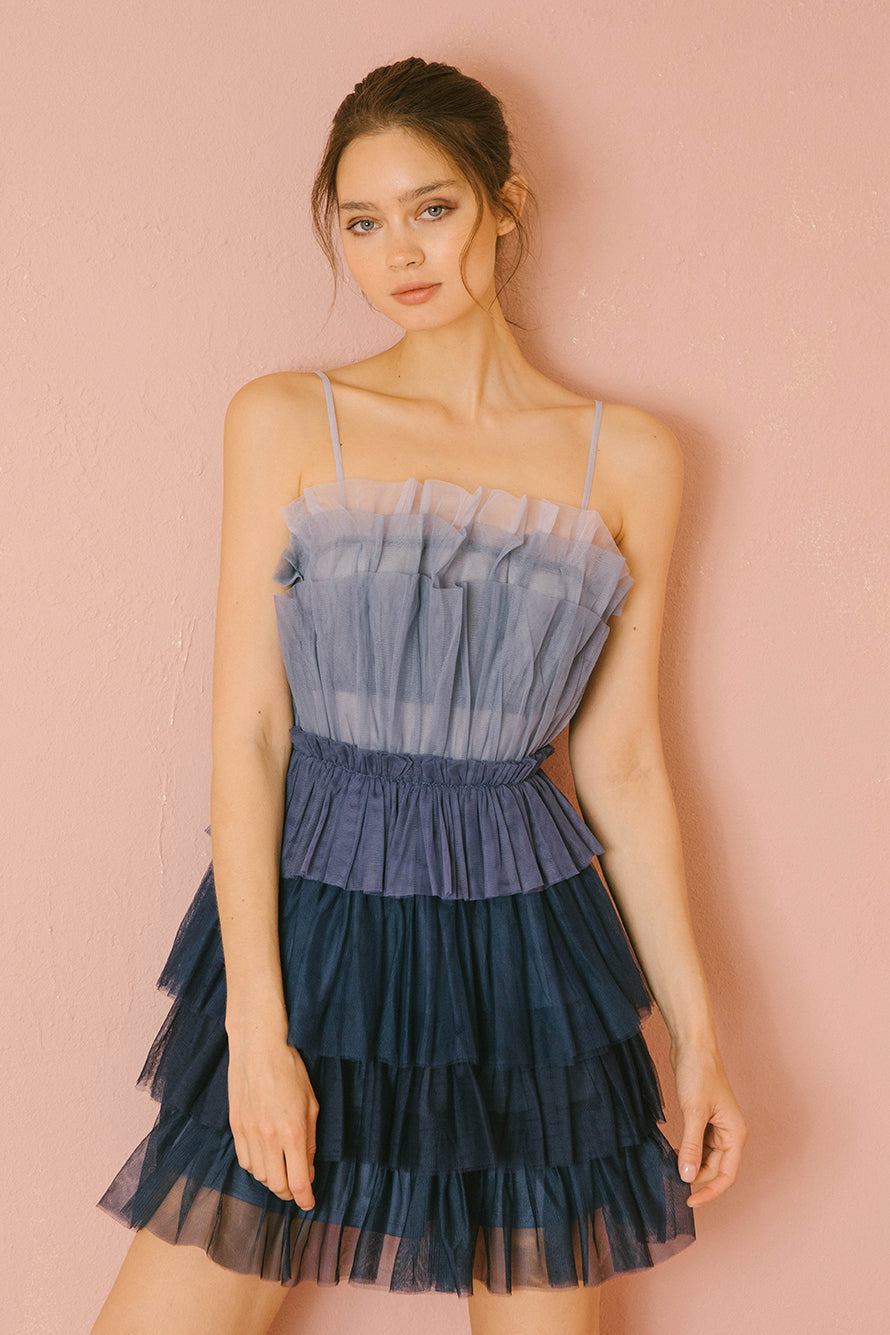 Woman wearing a blue ombre tulle tiered dress against a pink background
