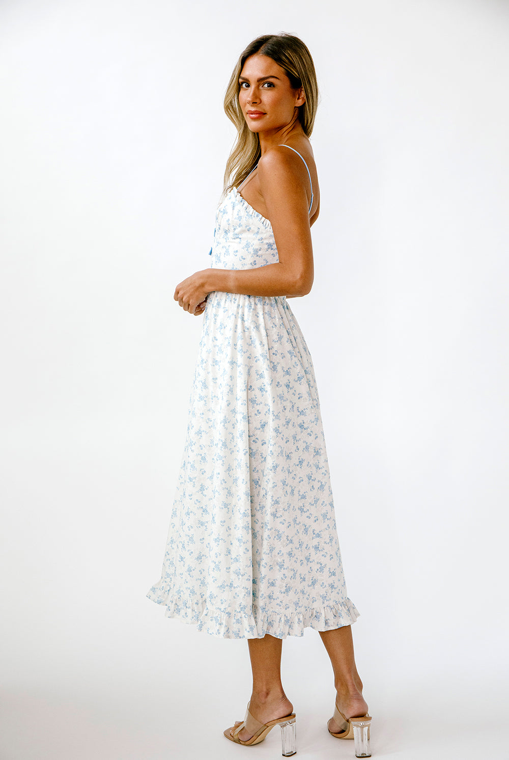 Side view of a woman wearing a white dress with blue floral patterns on a white background