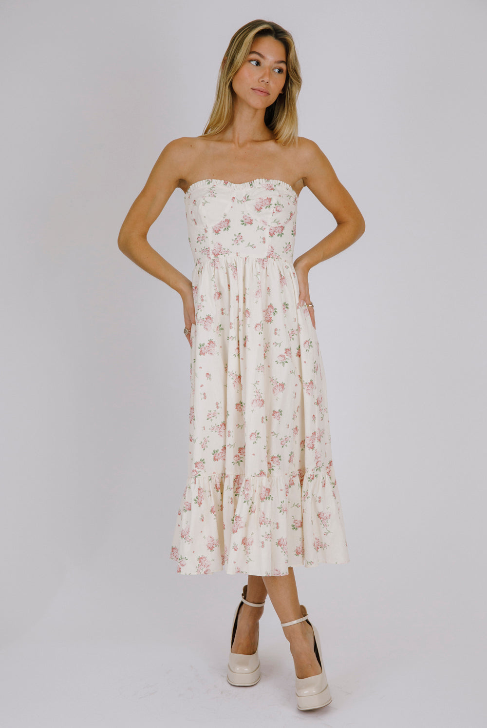 Woman wearing a strapless cream floral dress against a plain background