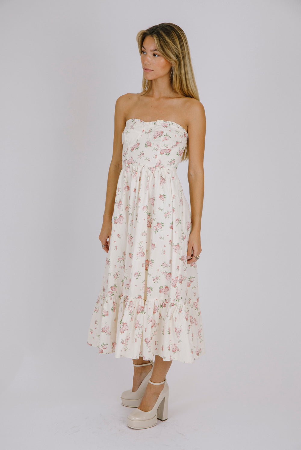Side view of a woman wearing a strapless cream floral dress against a plain background