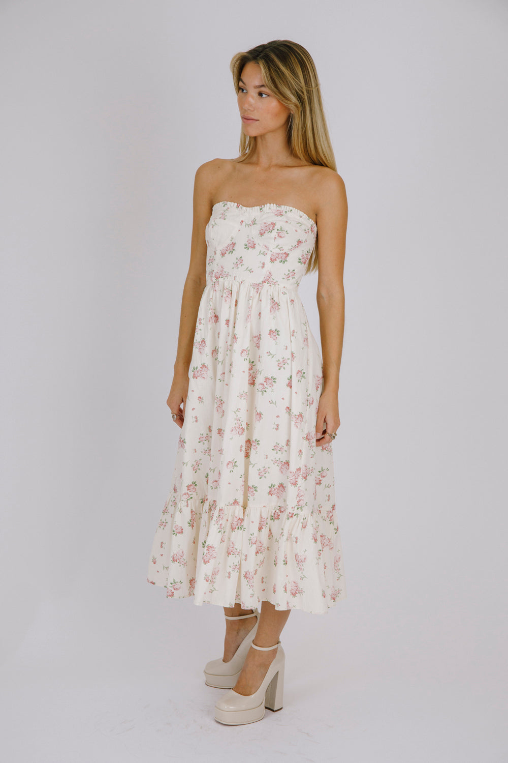 Side view of a woman wearing a strapless cream floral dress against a plain background