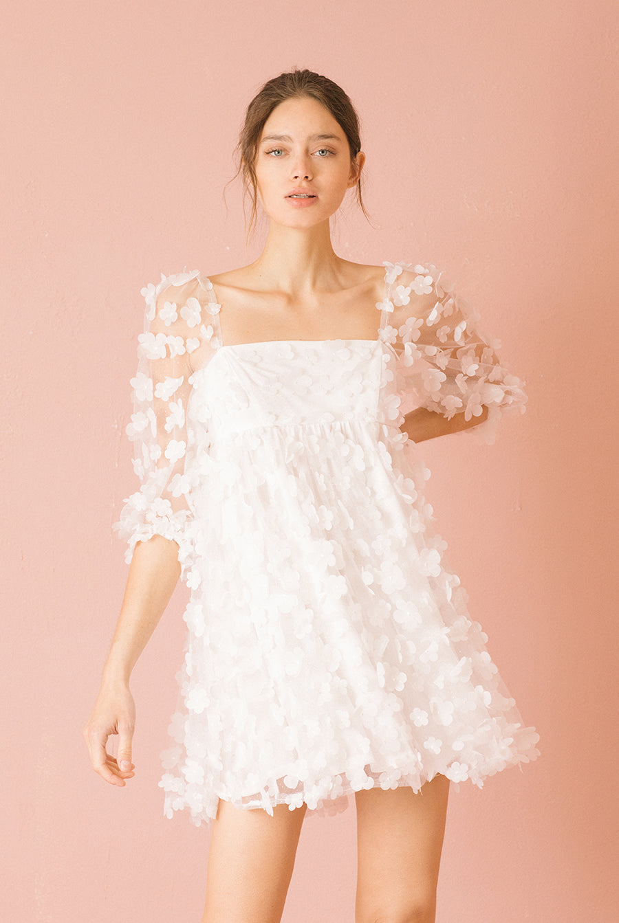 Woman wearing a white 3D floral mini dress against a pink background