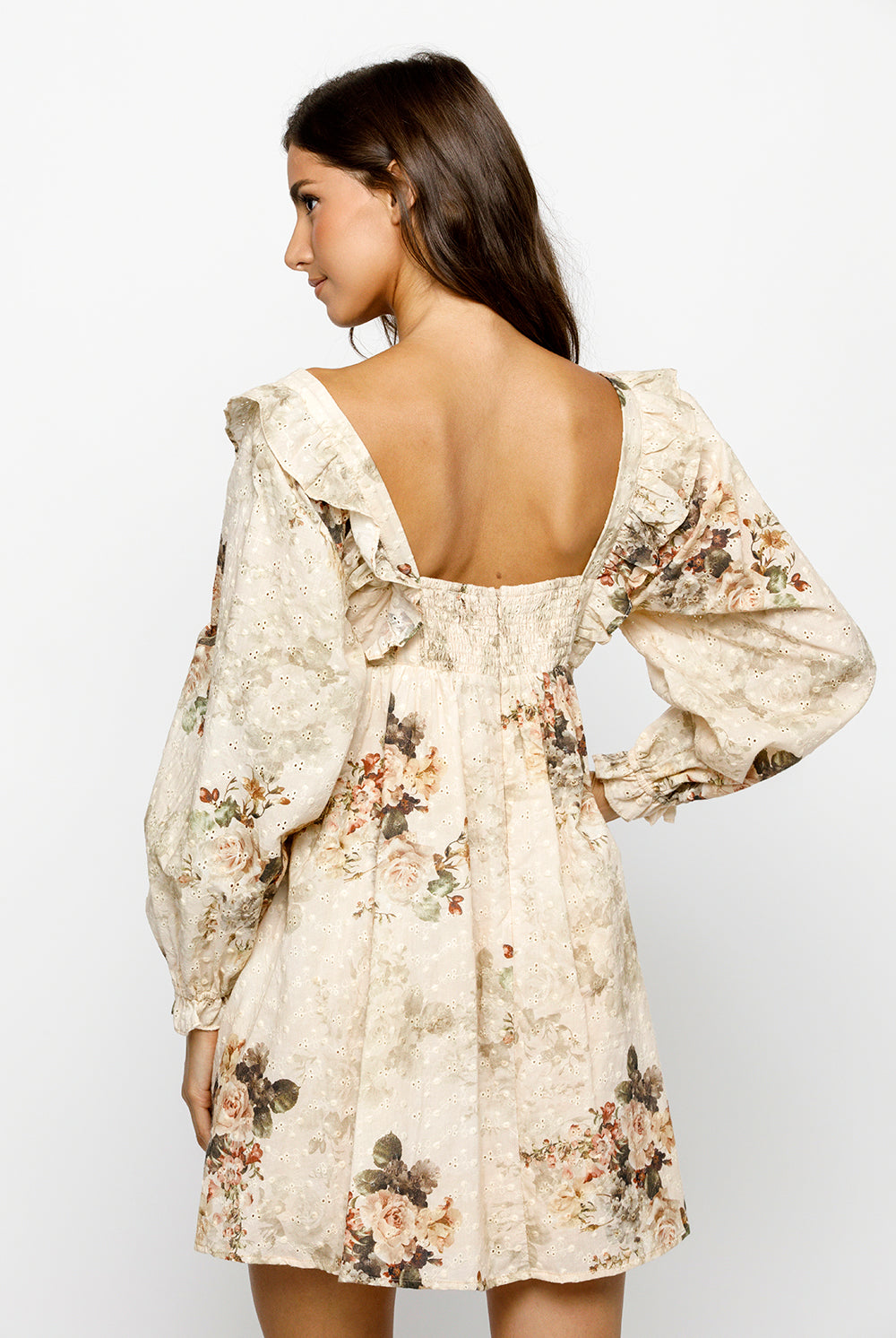 Back view of a woman wearing a beige floral dress with a plain background