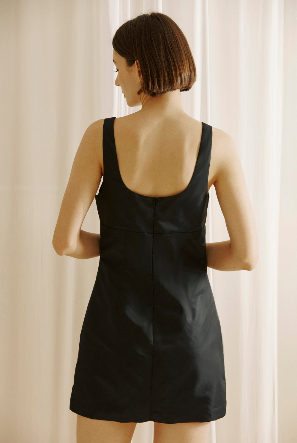 Back view of a woman wearing a black dress with a plain background