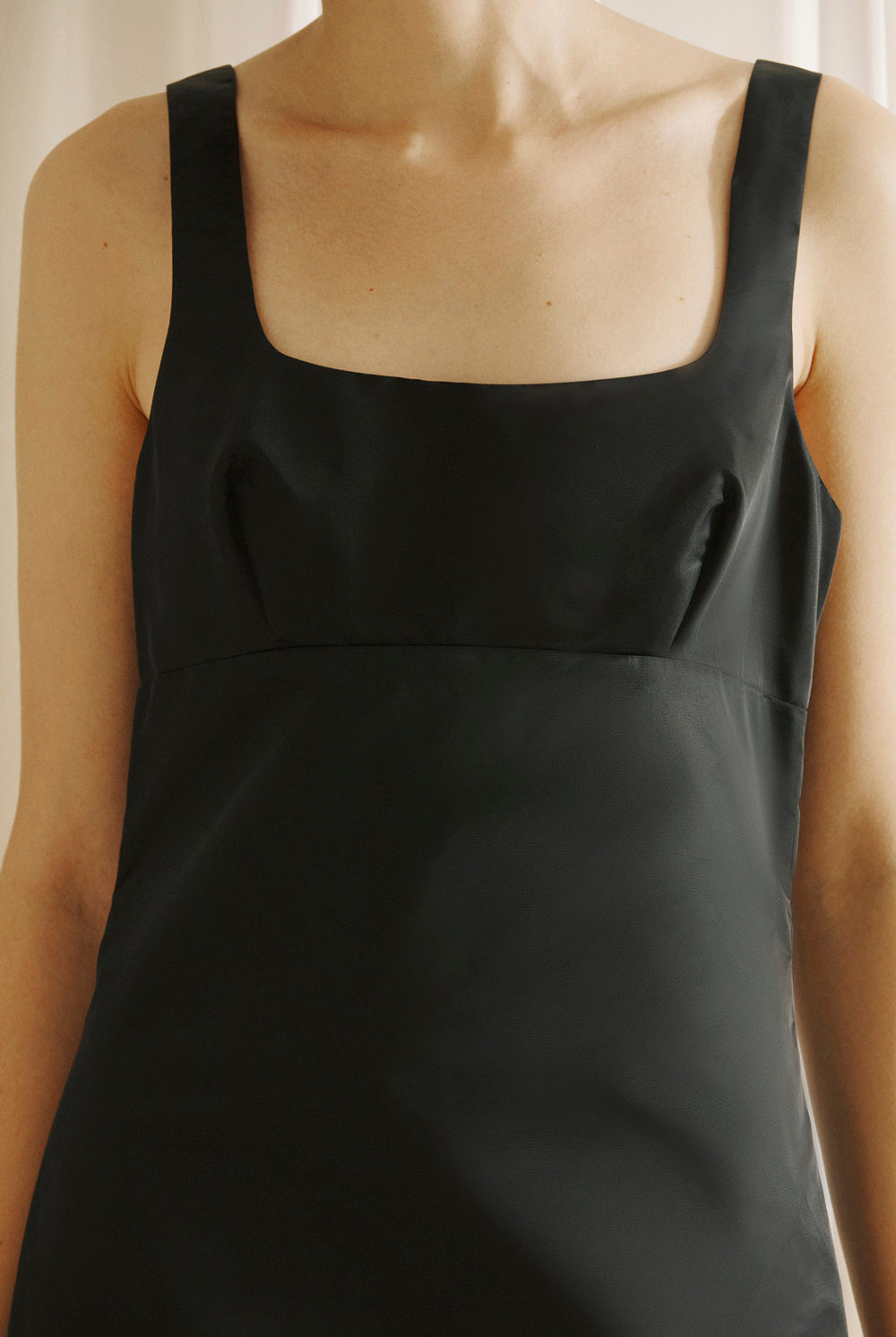 Black sleeveless dress worn by a person against a neutral background