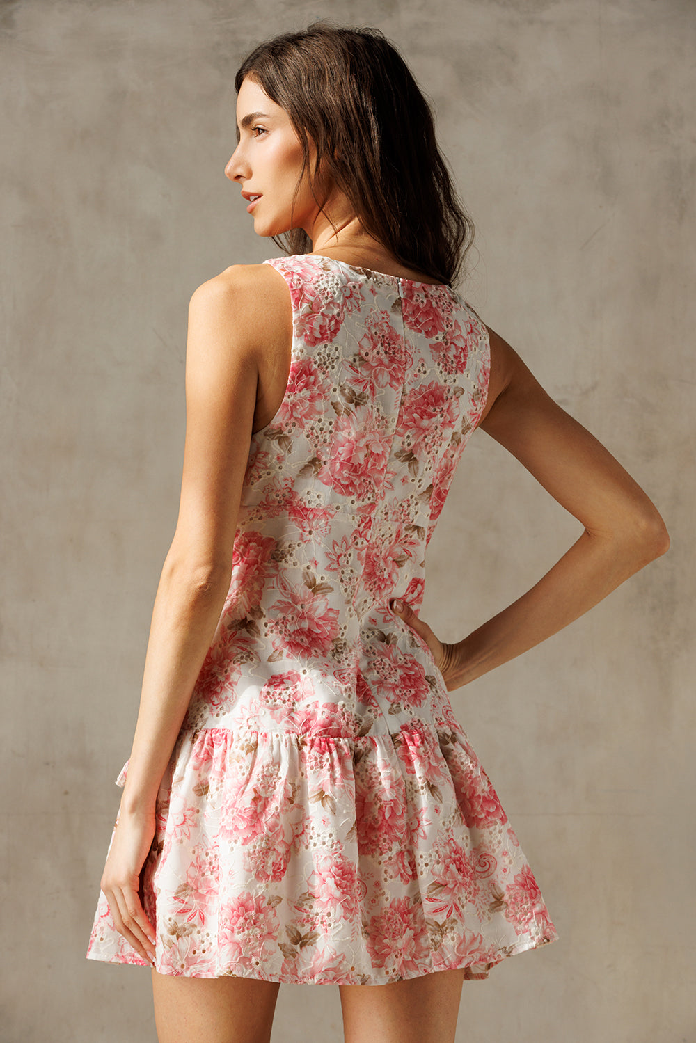 Back view of a woman wearing an ivory and pink floral dress against a plain background