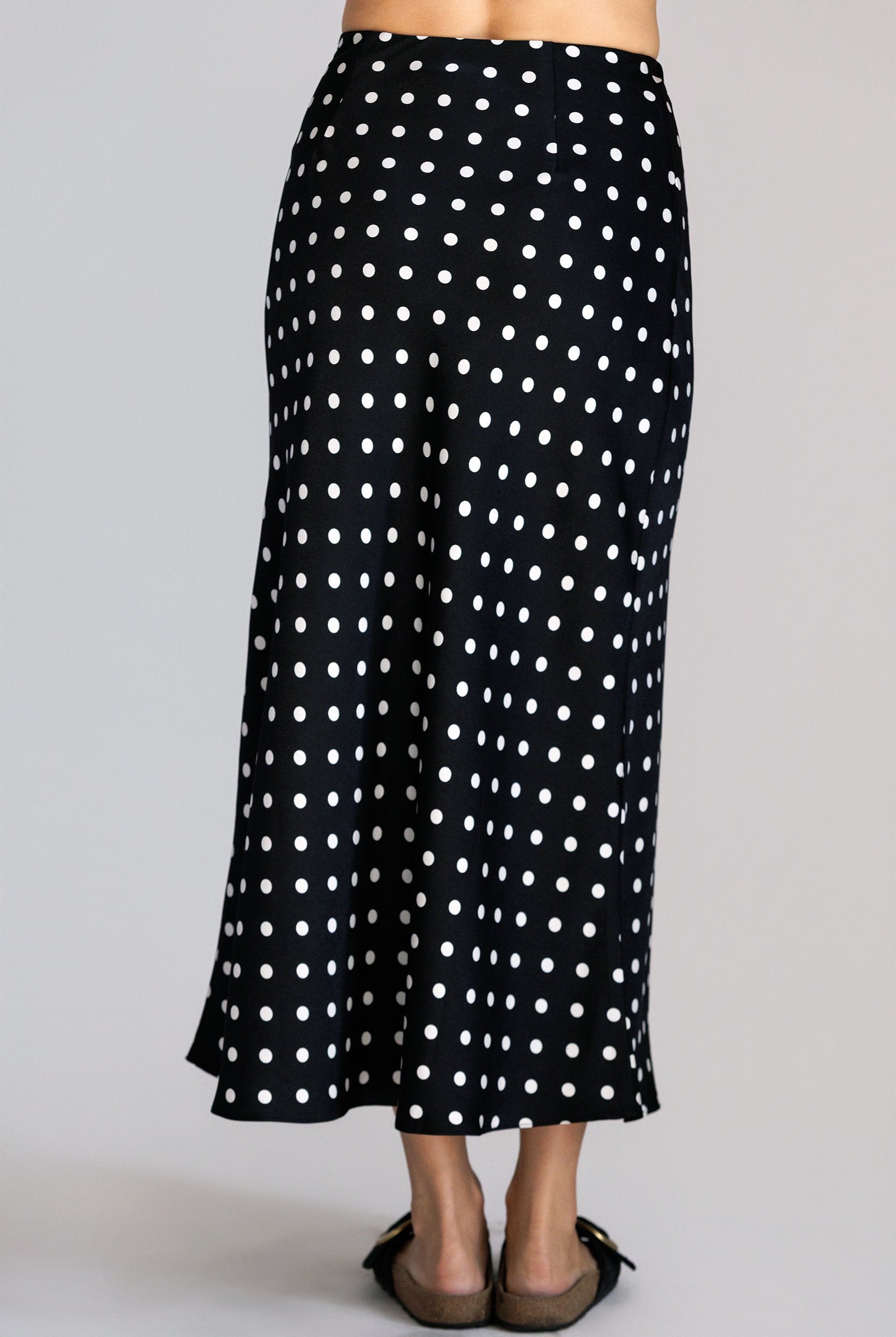 Back view of a black skirt with white polka dots worn by a person on a gray background