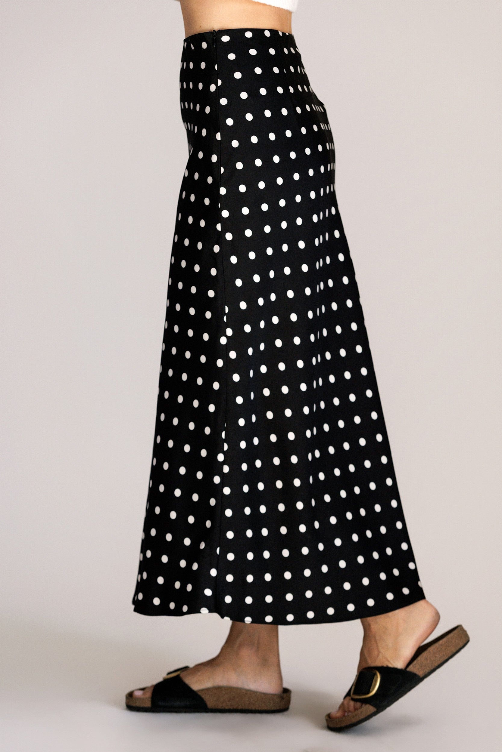 Side view of a black polka dot skirt worn by a person on a plain background