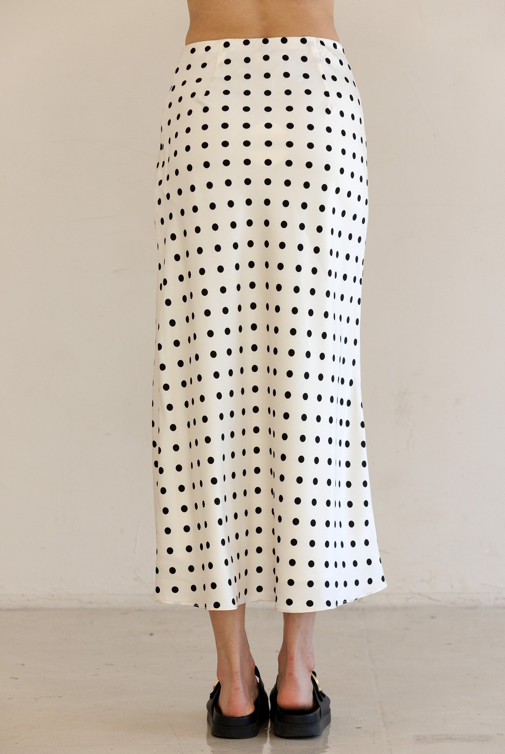 Person wearing a black and ivory polka dot skirt against a plain background