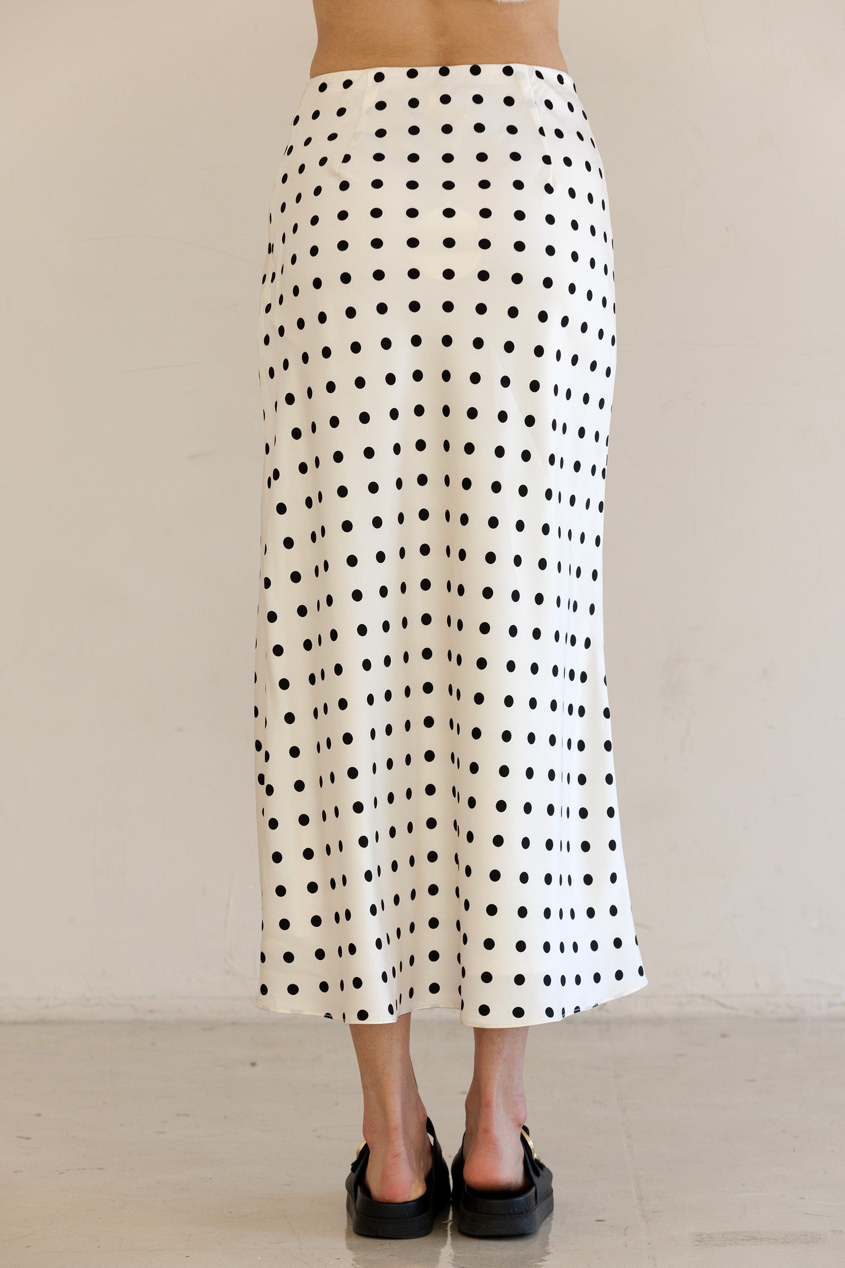 Person wearing a black and ivory polka dot skirt against a plain background