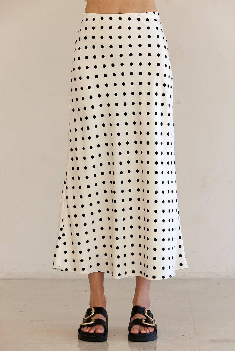 Person wearing an ivory polka dot skirt with a plain background