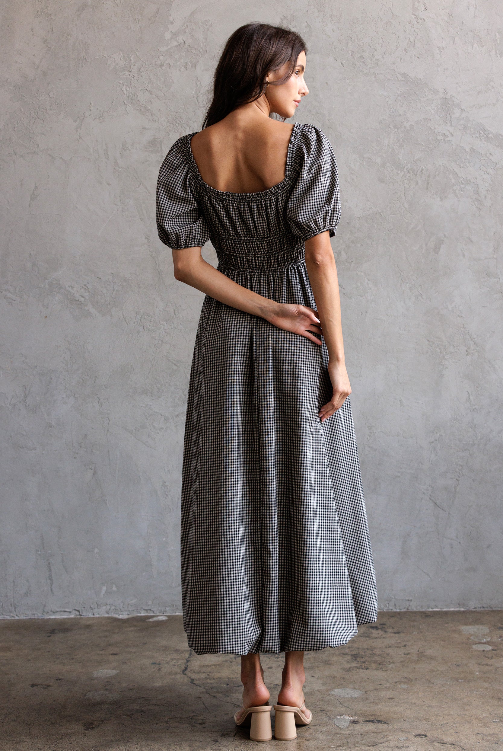 Woman wearing a checkered dress with puff sleeves against a gray concrete wall.