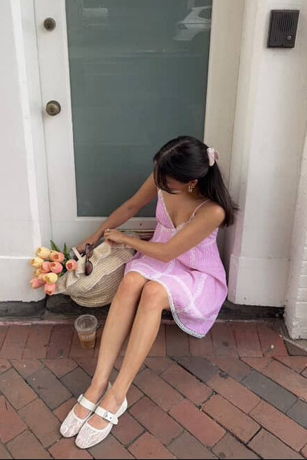 A woman in a pink striped dress sitting on a step outside a building.