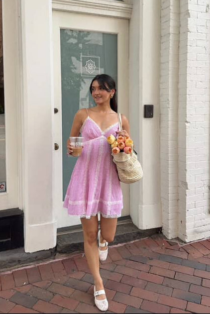 Woman in a pink striped dress standing on a sidewalk in front of a building